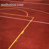 A sports court with a reddish-brown surface and bright yellow and white lines. The lines form geometric shapes, including rectangles and circles, suggesting markings for games like basketball or netball.