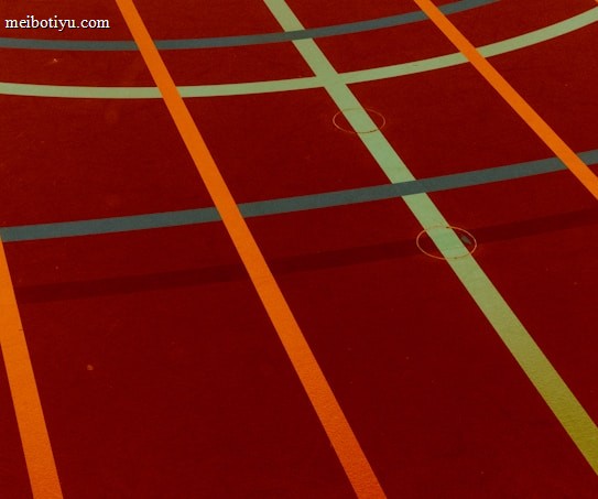 A sports court with intersecting lines in orange and blue, creating geometric patterns on a reddish-brown surface.